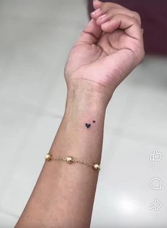 a woman's wrist with a small black heart tattoo on the left side of her arm