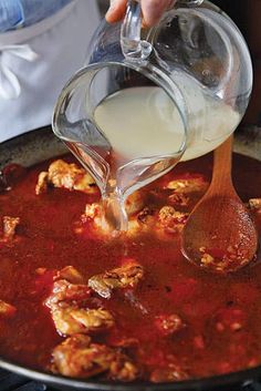 a person pouring milk into a pot filled with meat and tomato sauce on the stove