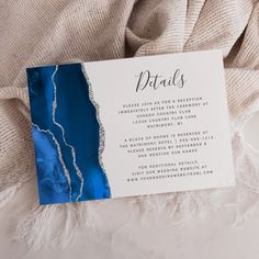 a blue and white wedding card with the words details on it sitting on a blanket