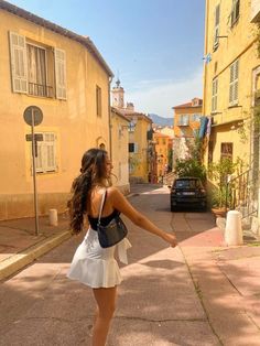 a woman in a white dress is walking down the street with her hand on her hip