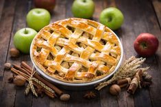 an apple pie sitting on top of a wooden table next to apples and cinnamon sticks