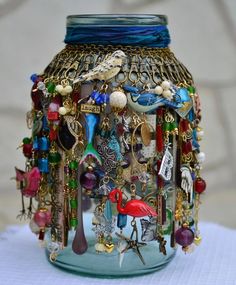 a glass jar filled with lots of different types of necklaces and charms on top of a table