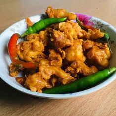 a white bowl filled with chicken and peppers on top of a wooden table next to a fork