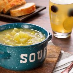 a bowl of soup sitting on top of a wooden table next to bread and drinks