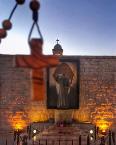 an image of a man holding a cross in front of a building with candles around it