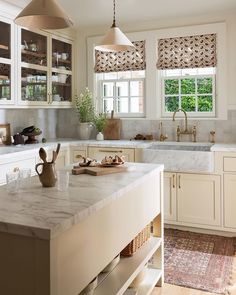 a kitchen with white cabinets and marble counter tops, two hanging lights above the sink