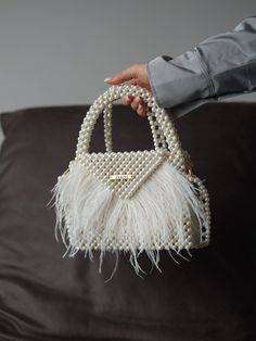 Exquisite Pearl Beaded Bag adorned with delicate ostrich feathers, a true statement piece for any occasion. Handcrafted with meticulous attention to detail, this luxury handbag exudes elegance and sophistication. Whether you're attending a wedding, a gala, or a special evening out, this pearl beaded bag is sure to turn heads and garner compliments. Its compact size makes it convenient to carry essentials such as your phone, keys, and lipstick, while the detachable beaded strap offers versatility in styling. 100% handmade Material: acrylic pearl beads 8 mm, ostrich feathers Size: > width - 20 cm | 8 in > height - 16 cm (26 cm with handle) | 6,3 in (10 inches with handle) > lateral width - 6 cm Lining: royal satin Includes 1 m | 40 inches beaded chain Gift wrapping and a satin pouch to store Pearl Beaded Bag, Pearl Purse, Hand Beaded Bag, Dating Gifts, Pearl Clutch, Crystal Bags, Purse Gift, Beaded Bag, Beaded Handbag