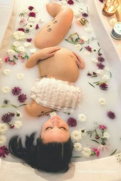 two women laying in a bathtub with flowers on the floor