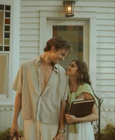 a man and woman standing in front of a house with a book on their lap