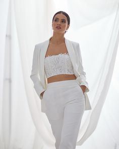 a woman in white pants and jacket walking down the runway with her hand on her hip