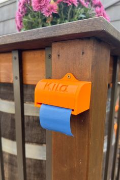 an orange mailbox with blue paper on it and pink flowers in the back ground