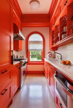 an orange kitchen with white counter tops and wooden floors, along with red cabinetry