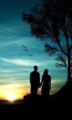 two people standing next to each other near a tree at sunset with birds flying in the sky