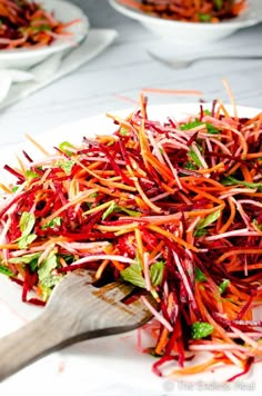 shredded carrots and lettuce on a white plate with a wooden serving spoon