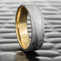 a gold and silver wedding band with an intricate design on the inside, sitting on a shiny surface