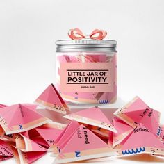 a jar filled with pink origami pieces next to a pile of pink paper