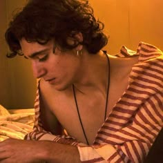 a man laying in bed looking at his cell phone while wearing a striped shirt and earrings