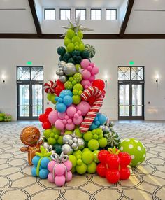 a christmas tree made out of balloons and other items in a room with large windows