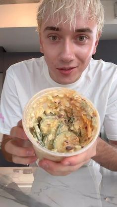 a young man holding up a bowl of food in front of his face and looking at the camera