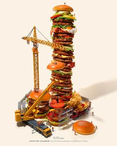 a very tall stack of hamburgers and other food items in front of a construction crane