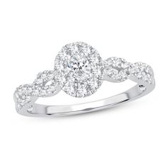 a white gold ring with an oval shaped diamond surrounded by small round brilliant cut diamonds