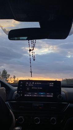 a car dashboard with a rosary hanging from it's dash board and the sun setting in the background