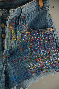 an old pair of jean shorts with colorful stitchs on them and buttons in the back pocket