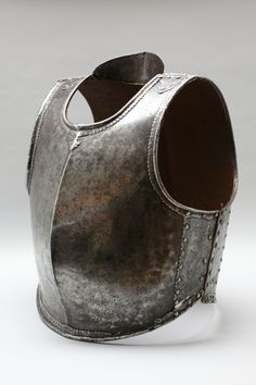 an old metal helmet with rivets on the front and side, sitting on a white surface