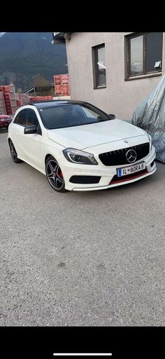 a white mercedes cla parked in front of a building next to a tarp