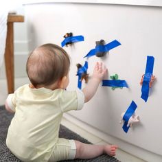 a baby sitting on the floor playing with blue tape and magnets that look like birds