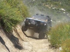 a black truck driving down a dirt road next to bushes and trees on top of a hill