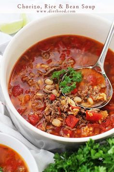 a white bowl filled with chili, rice and bean soup next to cilantro