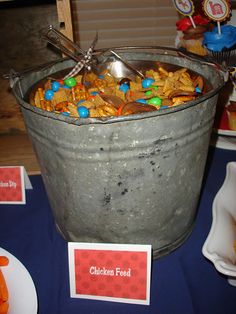 a bucket full of cheetos and candy sits on a blue tablecloth with place cards