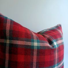 a red and black checkered pillow on a white surface with a light blue wall in the background