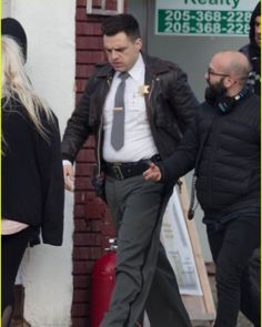 a man in a suit and tie walking down the street with other people behind him