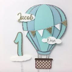 a blue hot air balloon cake topper with the number one on it's side