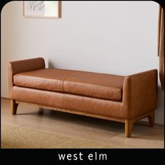 a brown leather couch sitting on top of a hard wood floor next to a window