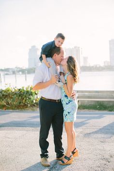 a man and woman kissing while standing next to each other in front of a body of water