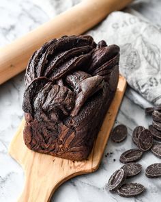 a loaf of chocolate cake sitting on top of a wooden cutting board next to cookies