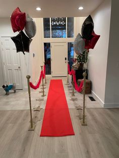 a red carpet with black and silver balloons on it in front of a white door