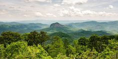 the mountains are covered in green trees and bushes, with clouds above them on a sunny day