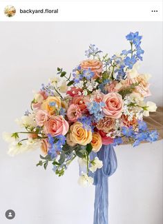 a blue ribbon tied around a bouquet of flowers on a white wall behind it is a vase with pink, orange and blue flowers