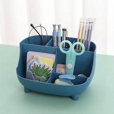 a blue desk caddy with pens, scissors and other office supplies in it on a table