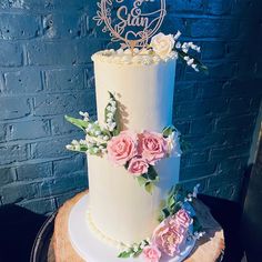 a three tiered cake with flowers and a heart topper on a wooden stand