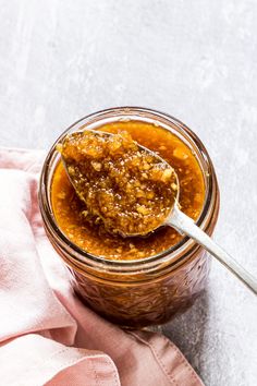 a spoon full of peanut butter on top of a pink napkin next to a jar filled with peanut butter