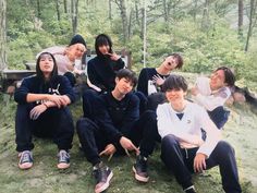 a group of young people sitting on top of a grass covered hillside in front of trees