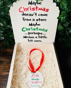 an open christmas gift box sitting on top of a wooden table next to greenery