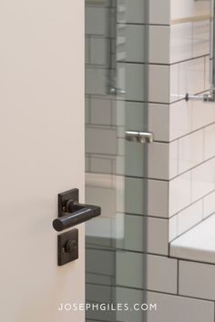 an open door to a bathroom with white tile and black handles on the handlebars