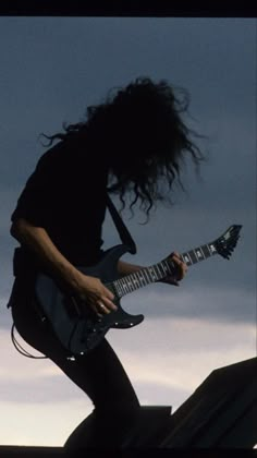 a man with long hair playing an electric guitar on top of a roof in the evening