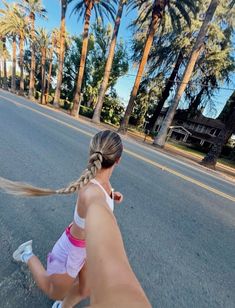 a woman riding a skateboard down a street next to palm trees